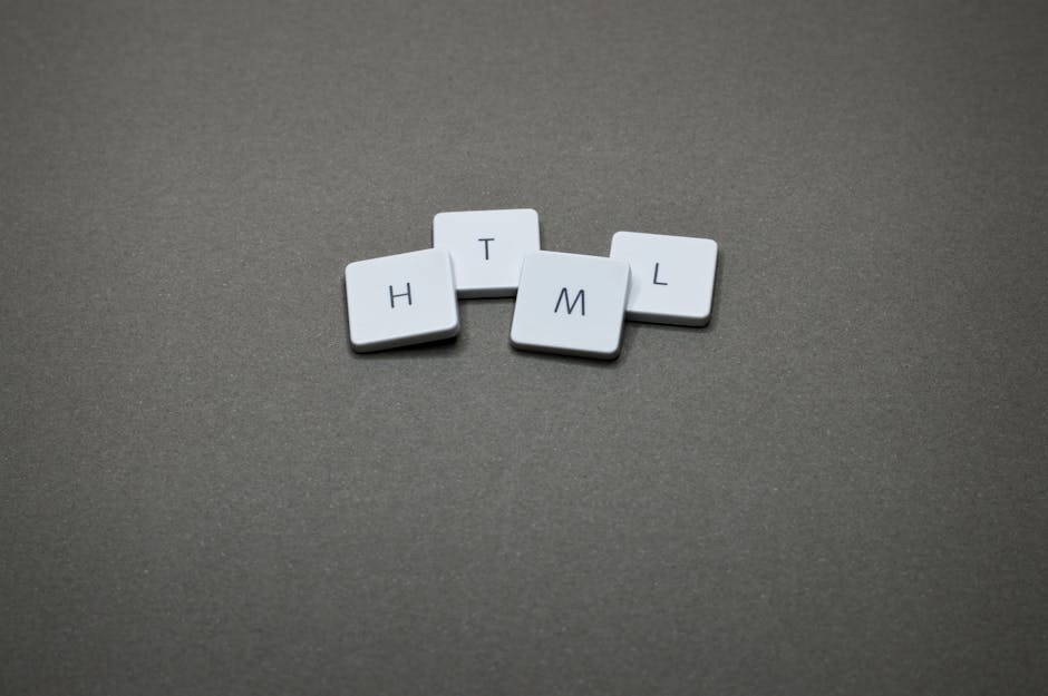Four white square tiles with black letters spelling 'H', 'T', 'M', and 'L' are arranged on a flat, grey textured surface. The tiles are positioned randomly, with some slight overlapping, and are situa